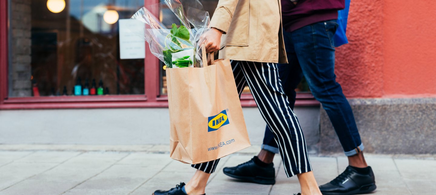 Two people walking, one holding an IKEA bag with a plant.