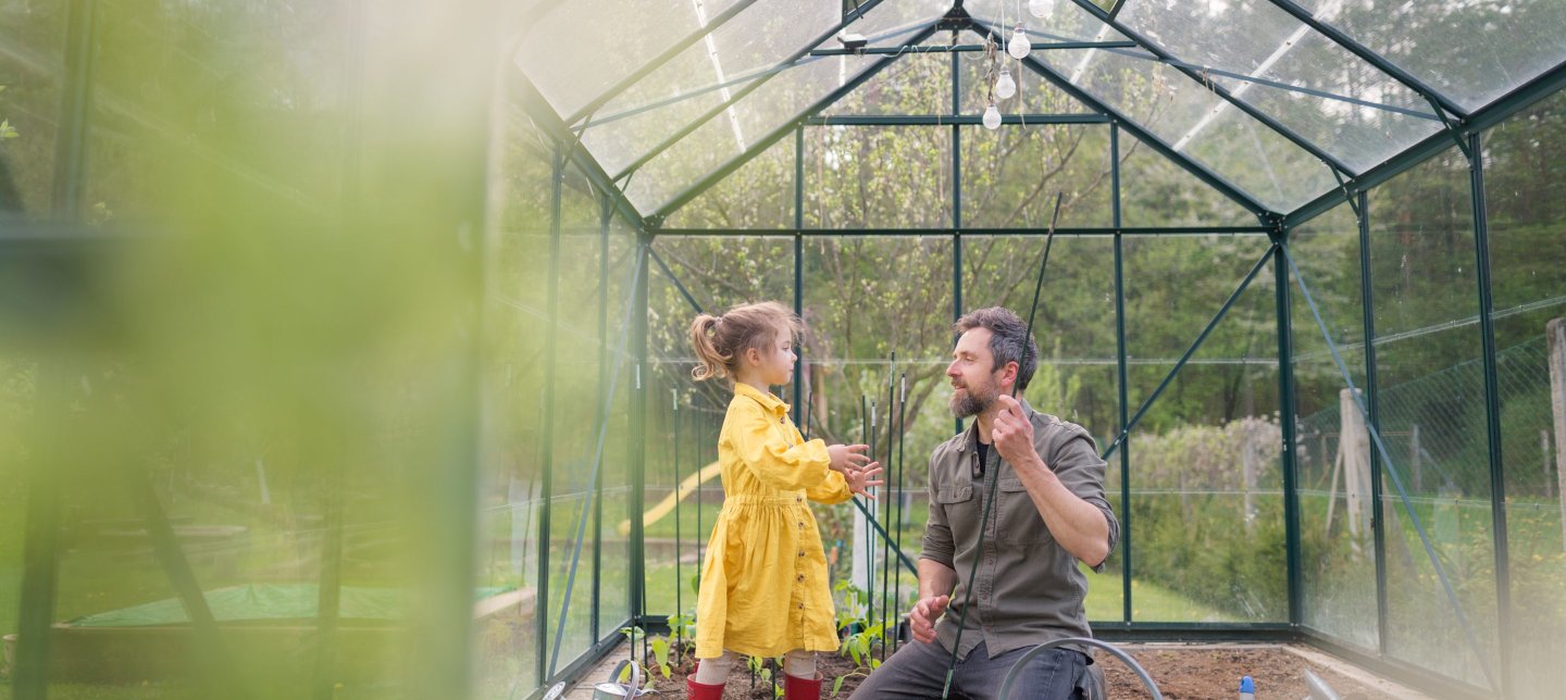 Father and daughter in a yellow dress and red rubber boots working together in a green house