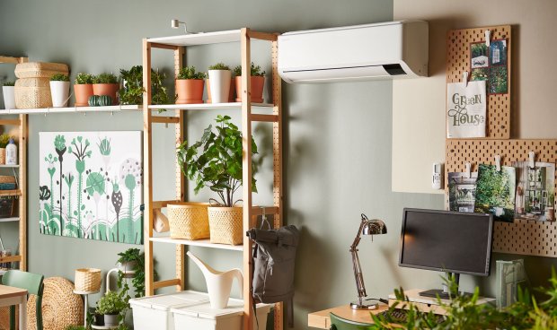 A living room with wooden book shelves, a desk and an air heat pump mounted on the wall.