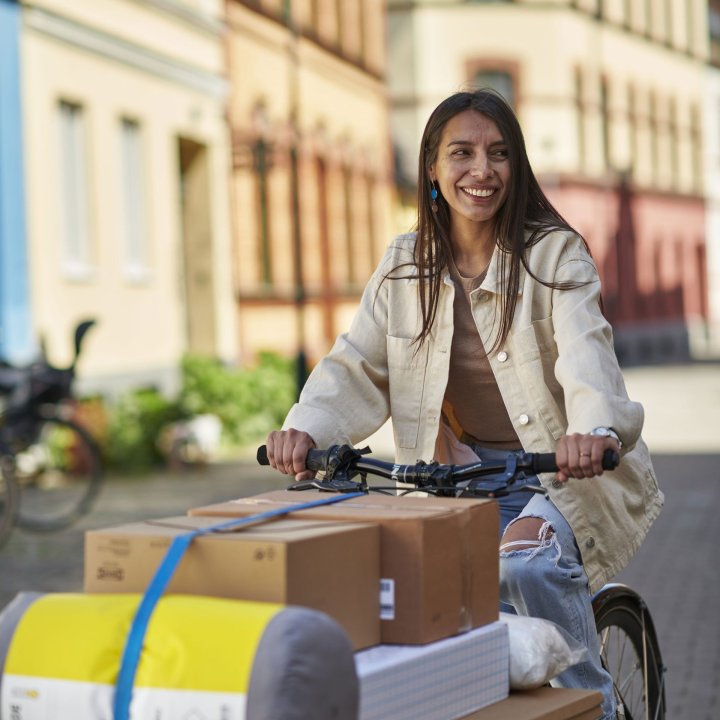 A smiling woman cycling on a cosy city street with IKEA packages stacked on her cargo bike.