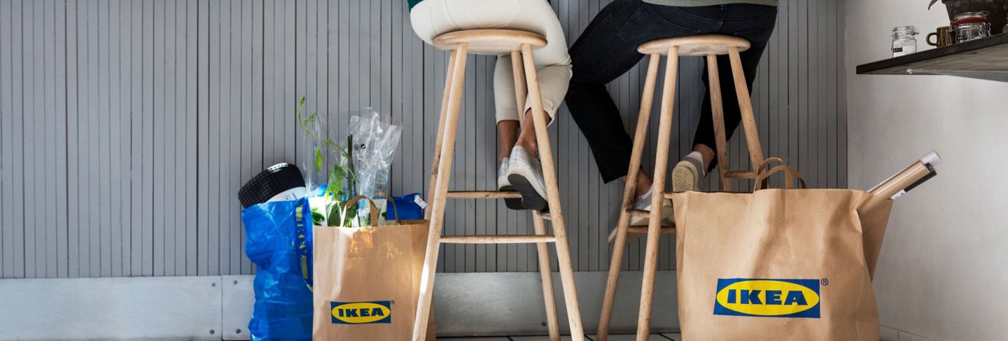 Two people sitting on stools with IKEA bags next to them