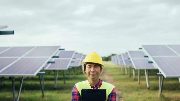 Woman in helmet and yellow west standing in front of solar panels
