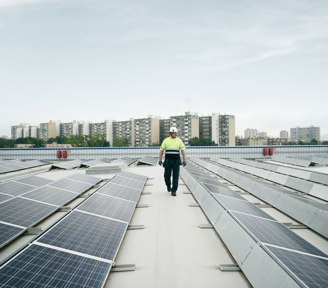 Man walking on a roof top with solar panels, high rise buildings in the background