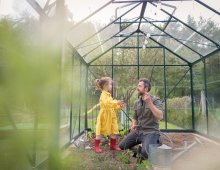 Father and daughter in a yellow dress and red rubber boots working together in a green house