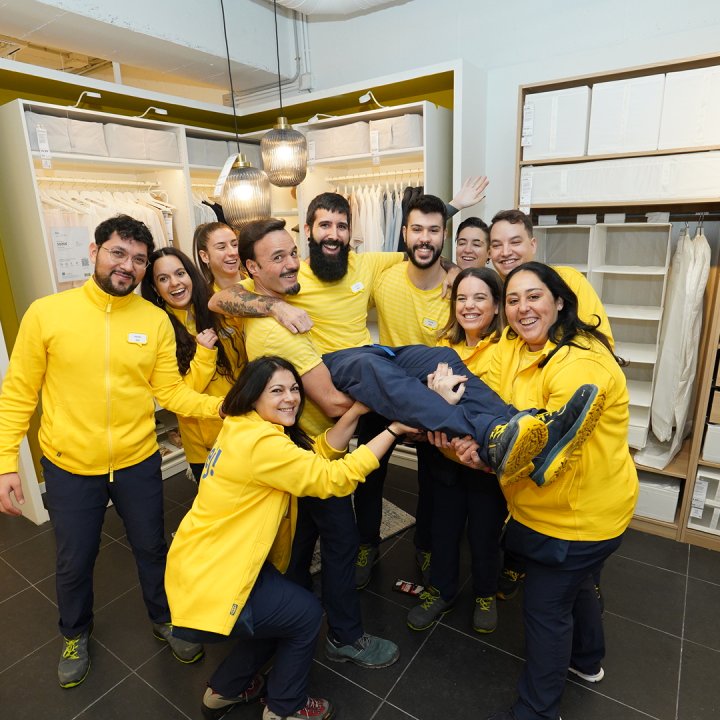 A group of IKEA employees in yellow sweaters carrying a colleague in their arms.